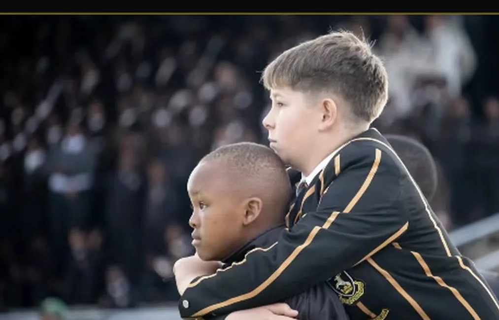 A Queen's College boy placing his arm around a younger boy at a rugby match